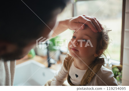Sick girl with fever and cold at home. Father touching little daughter forehead, checking her temperature. 119254095