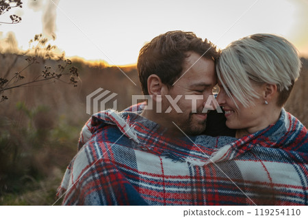 Couple in love on a walk in autumn forest. Husband and wife standing in the middle of meadow covered in warm blanket. 119254110