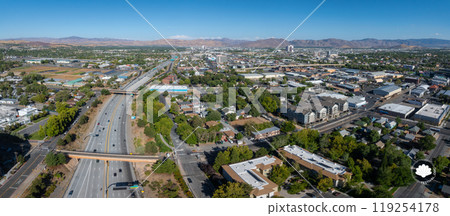 Aerial perspective of Reno, Nevada, featuring urban sprawl, a prominent highway, and surrounding mountains under a clear blue sky in daylight. Aerial perspective of Reno, Nevada, featuring urban sprawl, a prominent highway, and surrounding mountains under a clear blue sky in daylight. 119254178
