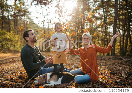 Young family with small children and dog on a walk in autumn forest. Throwing dry colorful leaves in the air. Young family with small children and dog on a walk in autumn forest. Throwing dry colorful leaves in the air. 119254179