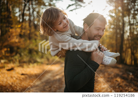 Father and girl are playful during walk in autumn forest. Dad and girl having fun outdoors. 119254186