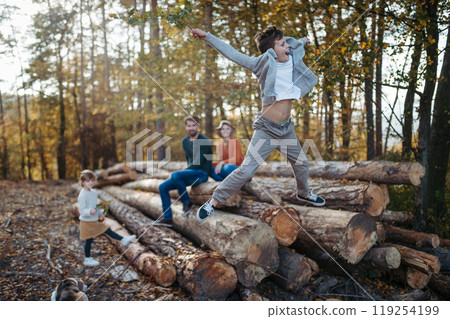 Portrait of family sitting on logs in the middle autumn forest, young boy jumping down, having fun. 119254199