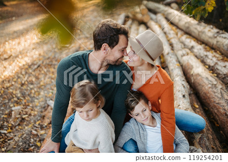 Portrait of family sitting on logs in the middle autumn forest. Nuclear family spending weekend outdoors. 119254201