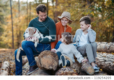 Portrait of family sitting in the middle autumn forest. Nuclear family with dog spending weekend outdoors. Portrait of family sitting in the middle autumn forest. Nuclear family with dog spending weekend outdoors. 119254205