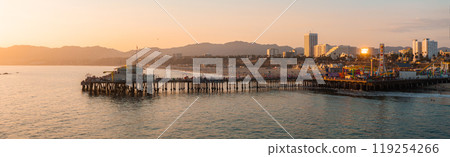 Santa Monica Pier extends into the Pacific Ocean, featuring a Ferris wheel and amusement park. The cityscape and mountains are visible in the background. 119254266