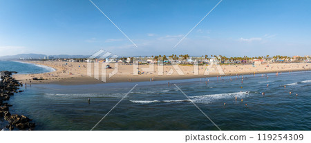 Panoramic aerial view of Venice Beach in Los Angeles, California, featuring sandy shores, Pacific Ocean waves, palm trees, and beachfront buildings. 119254309