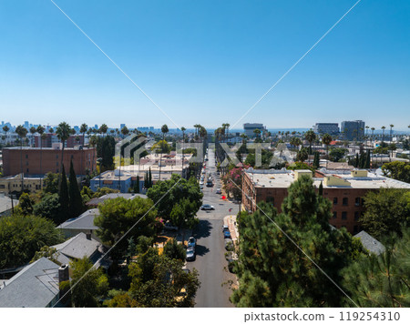 Aerial view of a Los Angeles residential area with palm lined streets, low rise buildings, and a distant skyline under a clear blue sky. 119254310