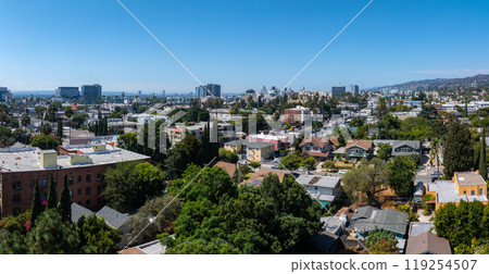 An aerial view of Hollywood's residential area in Los Angeles, featuring low rise buildings, lush greenery, and distant hills under a clear blue sky. An aerial view of Hollywood's residential area in Los Angeles, featuring low rise buildings, lush greenery, and distant hills under a clear blue sky. 119254507