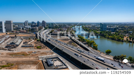 Aerial view of Sacramento, California, featuring a major highway, the Sacramento River with a bridge, and the iconic Ziggurat building under a clear sky. Aerial view of Sacramento, California, featuring a major highway, the Sacramento River with a bridge, and the iconic Ziggurat building under a clear sky. 119254509
