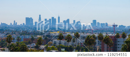 The image features Los Angeles skyline with downtown skyscrapers, palm trees, and mid rise buildings under a clear blue sky with visible construction cranes. 119254551