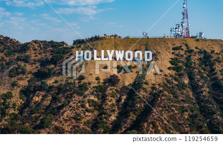 The Hollywood Sign is displayed on rugged hills with green patches, communication towers in the background, and a clear blue sky above in Los Angeles. The Hollywood Sign is displayed on rugged hills with green patches, communication towers in the background, and a clear blue sky above in Los Angeles. 119254659