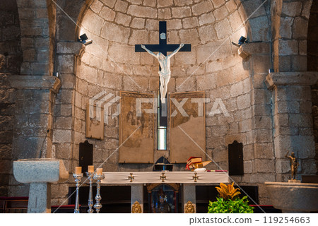 Explore the serene interior of a traditional Sardinian church, featuring a stone altar with a crucifix, framed artworks, and silver candlesticks. 119254663