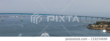 The Coronado Bridge arches over San Diego Bay, connecting to Coronado Island. Boats create trails in the water, with San Diego's skyline in the background. 119254690