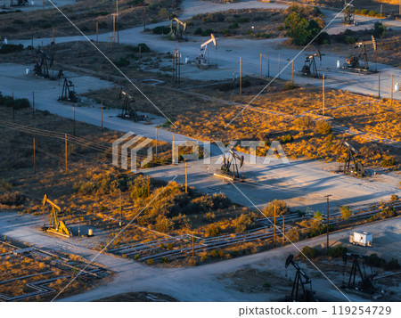 An aerial perspective of a California desert oil field, featuring active pumpjacks and pipelines. The barren terrain is dotted with scrub vegetation. 119254729