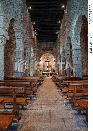 Explore the serene ambiance of a Romanesque church in Sardinia, featuring stone arches, vaulted ceilings, and a central altar with a prominent crucifix. 119254748