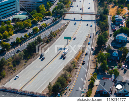 Aerial perspective of a highway in Reno, USA, featuring vehicles, a pedestrian bridge, residential houses, commercial buildings, and lush greenery. 119254777