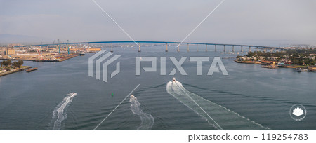 The San Diego Coronado Bridge spans the bay, with boats creating trails. Industrial areas and shipyards are on the left, greenery and urban areas on the right. The San Diego Coronado Bridge spans the bay, with boats creating trails. Industrial areas and shipyards are on the left, greenery and urban areas on the right. 119254783