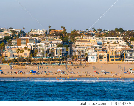 Manhattan Beach in California features a sandy beach with colorful umbrellas and beachgoers. Residential buildings and palm trees line the background. Manhattan Beach in California features a sandy beach with colorful umbrellas and beachgoers. Residential buildings and palm trees line the background. 119254789