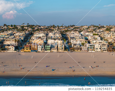 Scenic aerial view of Manhattan Beach, Los Angeles, showing sandy beach, beachgoers, volleyball courts, Pacific Ocean waves, and residential homes. 119254835