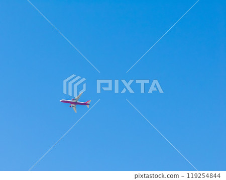 A red and white airplane is captured in flight against a clear blue sky, creating a minimalist composition with no visible landmarks or features. 119254844