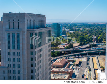 Aerial perspective of Sacramento, California, featuring a modern high rise, highways, lush greenery, urban structures, and distant hills under a clear sky. Aerial perspective of Sacramento, California, featuring a modern high rise, highways, lush greenery, urban structures, and distant hills under a clear sky. 119254860