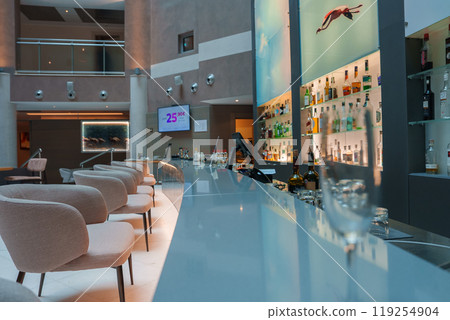 Modern bar in a Sardinian luxury hotel featuring plush seating, illuminated bottle display, and unique diving artwork, creating a sophisticated ambiance. 119254904