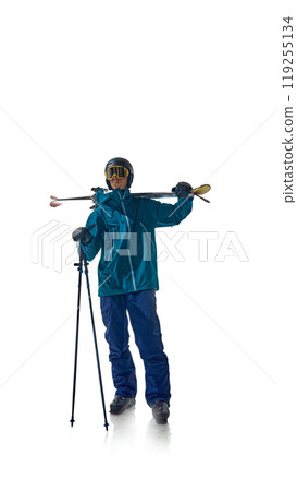 Skier dressed in teal gear stands confidently with his ski poles, ready for action against white studio background. He stares ahead, exuding focus and preparation. 119255134
