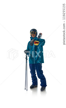 Skier dressed in teal gear stands confidently with his ski poles, ready for action against white studio background. He stares ahead, exuding focus and preparation. 119255135