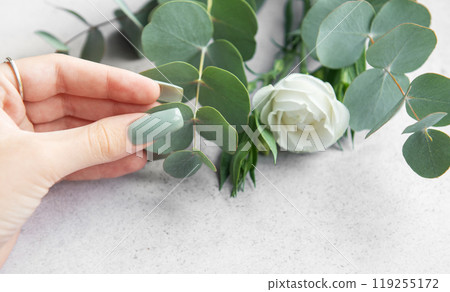 A hand gently touches eucalyptus leaves while preparing a floral arrangement with A hand gently touches eucalyptus leaves while preparing a floral arrangement with 119255172