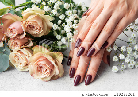 Elegant hands with dark manicure resting beside blush roses and white blooms on a light surface Elegant hands with dark manicure resting beside blush roses and white blooms on a light surface 119255201