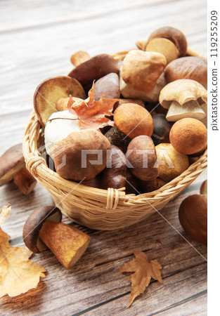 A woven basket filled with various mushrooms and autumn leaves on a wooden surface 119255209