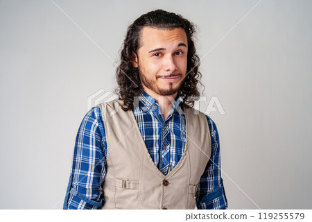 Young man in plaid shirt and vest poses confidently against a neutral background 119255579