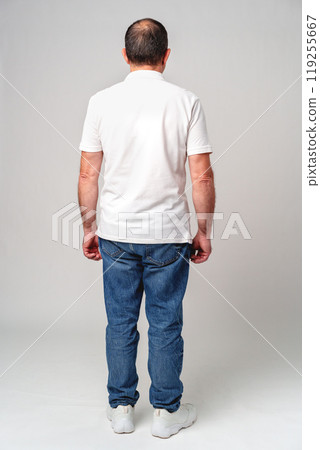 Man standing alone in casual attire, facing away, in a minimalistic indoor setting Man standing alone in casual attire, facing away, in a minimalistic indoor setting 119255667