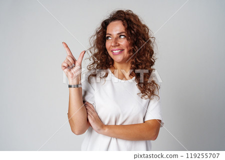 A young woman with curly hair playfully pointing finger while standing against a gray background A young woman with curly hair playfully pointing finger while standing against a gray background 119255707