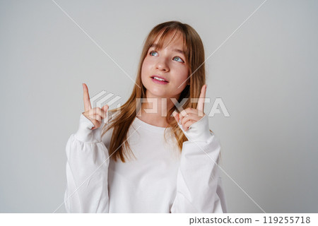 Young girl in a white sweater pointing against a plain background 119255718