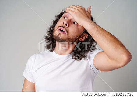 A man with curly hair expresses surprise while looking upwards in a neutral background A man with curly hair expresses surprise while looking upwards in a neutral background 119255723