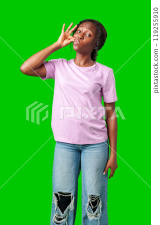 A young woman in a pink shirt makes a shushing gesture against a bright green background A young woman in a pink shirt makes a shushing gesture against a bright green background 119255910