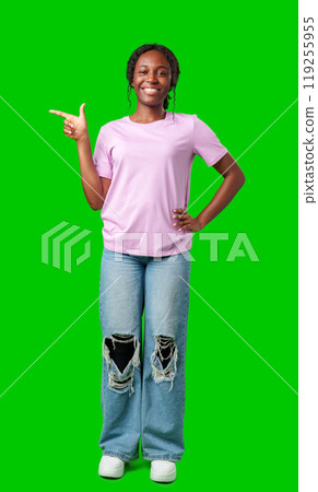 A young girl stands confidently pointing to the right against a bright green backdrop A young girl stands confidently pointing to the right against a bright green backdrop 119255955