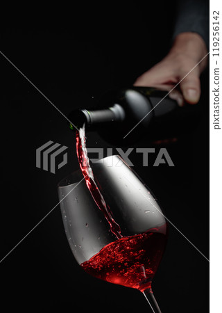 Pouring red wine in a glass goblet. 119256142
