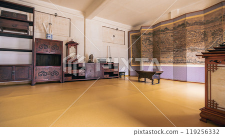 Traditional Korean interior room with wooden furniture and detailed folding screen depicting historical landscape. The room features ornate cabinets and shelves, showcasing Korean craftsmanship. Traditional Korean interior room with wooden furniture and detailed folding screen depicting historical landscape. The room features ornate cabinets and shelves, showcasing Korean craftsmanship. 119256332