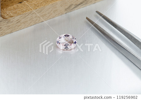 macro mineral faceted stone Morganite with tweezers on a gray background 119256902