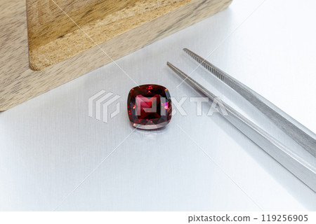 macro mineral faceted stone Garnet with tweezers on a gray background macro mineral faceted stone Garnet with tweezers on a gray background 119256905