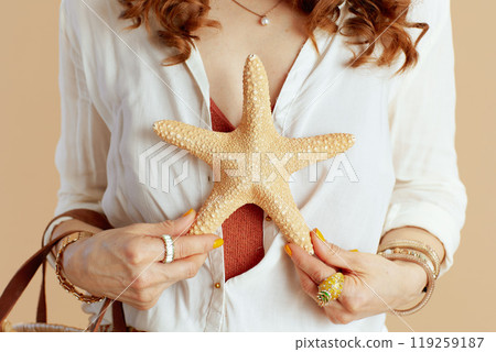 Trendy woman in blouse and shorts with sea star on beige 119259187