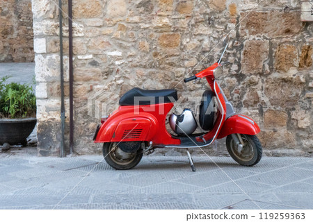 A red Vespa stands out against the backdrop of a medieval village in Italy. A red Vespa stands out against the backdrop of a medieval village in Italy. 119259363