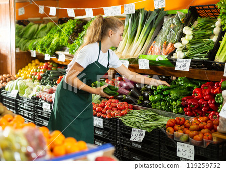 Focused girl who works part-time as a trainee saleswoman puts pepper on showcase 119259752