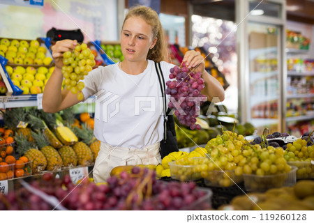 Portrait of a fifteen-year-old girl chooses grapes, holding bunches 119260128