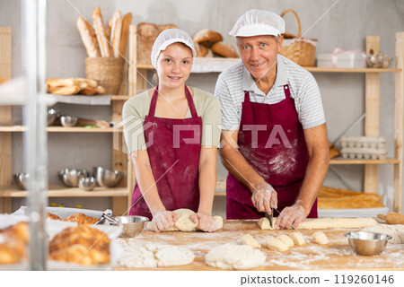 Grandfather and granddaughter working together with dough in family bakery 119260146