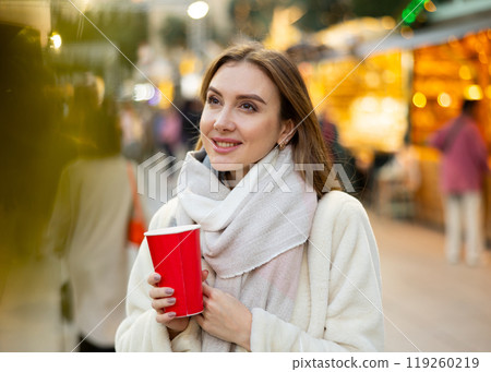 Young woman stands with glass of hot coffee in her hands and enjoys festive New Year atmosphere Young woman stands with glass of hot coffee in her hands and enjoys festive New Year atmosphere 119260219