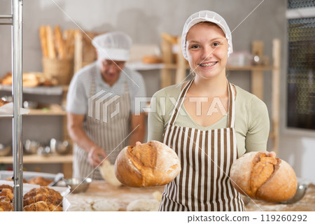 Bakery girl employee holds ready-made loafs of bread. 119260292