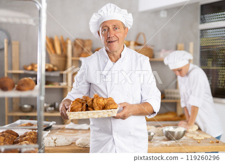 Elderly man baker with basket of croissants 119260296